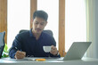 © wattana - Successful young businessman drinking coffee and checking financial reports at office desk.