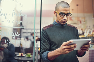 Aufkleber - Keeping an eye on his competition. Shot of a man using his digital tablet while standing in the entrance of a cafe.