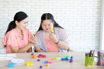 Wall Mural - down syndrome girl with woman teacher learning to use colorful and play dough on a table