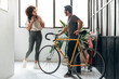 © Daniel - Multiracial friends meet at co working office entrance. Caucasian man leaving with a bike, woman arrives at work.