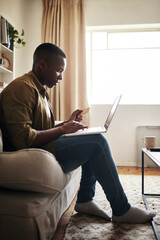 Poster - I work too hard to not spoil myself.... Full length shot of a handsome young man using a laptop and a credit card to shop online while sitting on his couch at home.