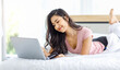 © Bangkok Click Studio - Asian young happy cheerful beautiful female model in casual pajama outfit lying down smiling hold credit card on bed in bedroom browsing surfing internet shopping online via laptop notebook computer