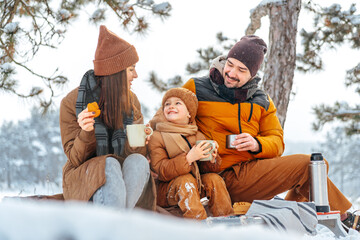 Happy family with cups of hot tea spending time together in winter forest