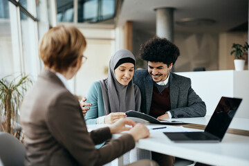 Wall Mural - Young Middle Eastern couple having consultation with their real estate agent during meeting in the office.