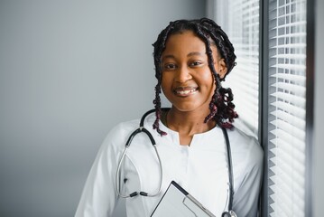 Wall Mural - Portrait confident African female doctor medical professional writing patient notes isolated on hospital clinic hallway windows background. Positive face expression