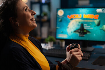 Canvas Print - Happy woman using joystick to play video games on computer. Gamer winning online games with controller in front of monitor. Person feeling cheerful and celebrating win on internet.