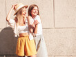 © halayalex - Two young beautiful smiling hipster female in trendy summer clothes.Sexy carefree women posing in the street near white wall in hat. Positive pure models having fun at sunset