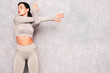 © halayalex - Fitness confident woman in sports clothing. Sexy young beautiful model with perfect body. Female posing near grey urban wall in studio. Stretching out before training