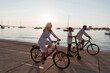 © .shock - Happy family enjoying a beautiful morning by the sea together, parents riding a bike and their son riding an electric scooter. Selective focus