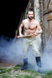 sexy shirtless man standing in front of barn with a pickaxe