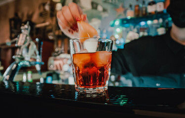 Closeup shot of bartender hand making negroni cocktail. Negroni classic cocktail and gin short drink with sweet vermouth, red bitter liqueur and dried orange garnish.