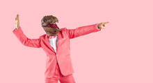 Funny Goofy Guy Having Fun In The Studio. Happy Energetic Excited Crazy Man Wearing Stylish Funky Vibrant Pink Party Suit And Dinosaur Mask Dancing And Pointing Finger Away Isolated On Pink Background