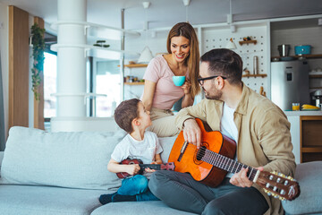 Wall Mural - Father teaching his son how to play guitar. Mom watching. Dad playing some music on a guitar to his son. Playing his favorite song. Father Teaching Son Guitar