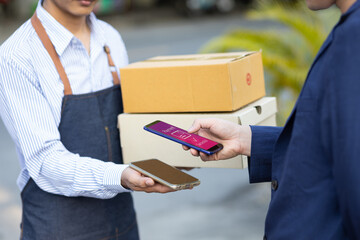 Man uses mobile phone to confirm payment before picking up parcel from delivery man.