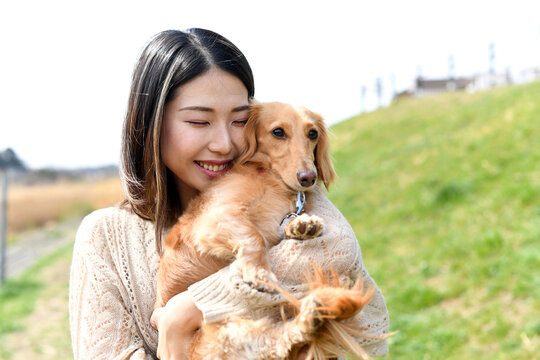 屋外で愛犬（ミニチュアダックスフンド）を抱っこする若い女性