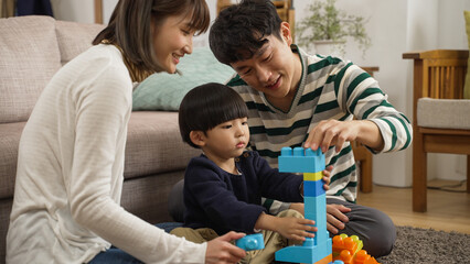 Wall Mural - happy japanese family of three enjoying playing plastic building blocks in the living room at home. the father is helping hold the unstable bricks for his son to prevent them fall