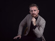 © .shock - Portrait of adult businessman wearing trendy suit and sitting in modern studio on stylish chair against the black background