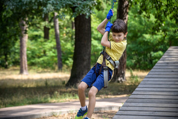 Wall Mural - Strong excited young boy playing outdoors in rope park. Caucasian child dressed in casual clothes and sneakers at warm sunny day. Active leisure time with children concept