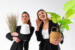 © Andrii - Two young business woman dressed black suit smile holding houseplant and lamp standing isolated on white background. Moving concept. Relocation new office with positive.