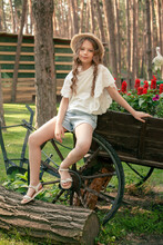 Carefree Tween Girl Sitting On Old Wooden Cart Decorated As Flowerbed At Country Estate In Forest