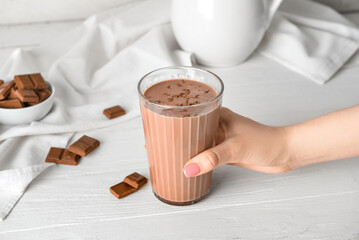 Wall Mural - Female hand holding glass of delicious chocolate milk on white wooden background