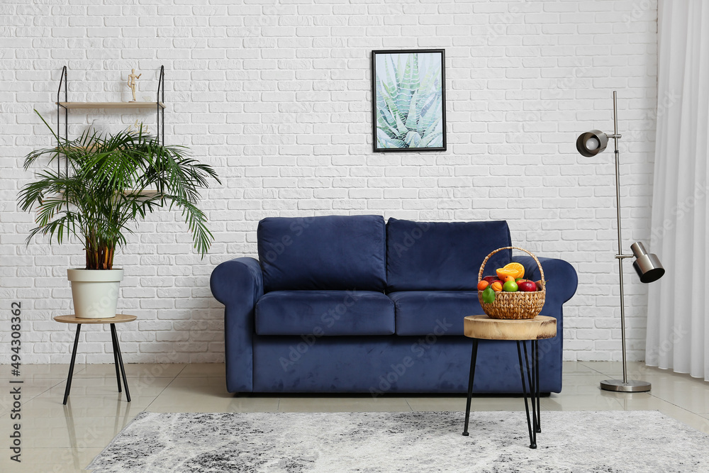 Interior of light living room with blue sofa, stool and fruit basket