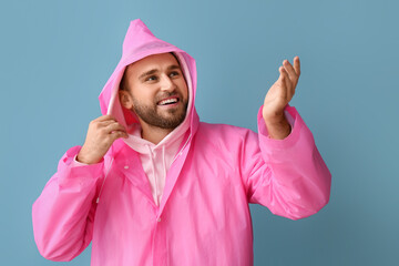 Wall Mural - Young man in stylish raincoat showing something on color background