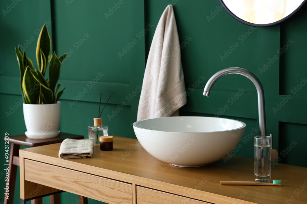 Table with sink and bath supplies near green wall