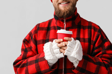 Wall Mural - Young bearded man in warm gloves with cup of coffee on light background, closeup