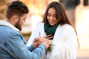 Wall Mural - Young man putting ring on finger of his fiancee after marriage proposal in park