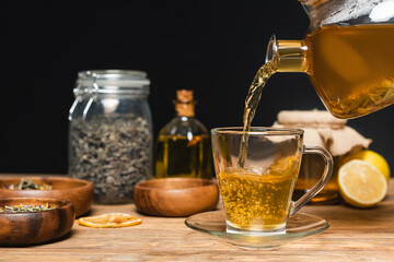 Canvas Print - Teapot near cup, blurred honey and lemons on wooden surface isolated on black.