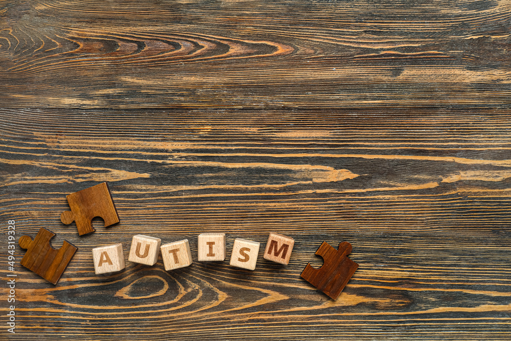 Word AUTISM with puzzle pieces on dark wooden background