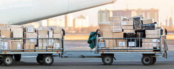 Close-up detail view of cargo cart trolley full with commercial parcels against turboprop cargo plane. Air mail shipping and logistics. Import export operations. Commercial charter flight service