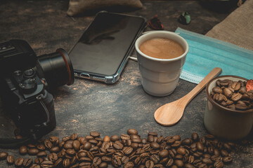 Canvas Print - Closeup shot of a cup of coffee, beans, a mobile phone, a camera and a medical mask