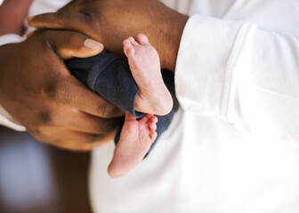 Wall Mural - Beautiful close-up shot of a newborn baby bare feet and a black male hands holding the  baby