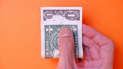 Man's hand is making a payment. Business Investment Economy Saving Loan Income Money and Finance concept. Male hand showing dollar cash on an orange background. One Dollar 1 USD. Prosperity concept.