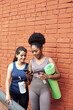 © etonastenka - Image of amazing young athletic women in front of a brick wall, looking into the phone. Two female friends laugh at the social media post