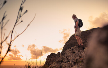 Older man adventurous hiker standing on mountain cliff looking out at the view. 