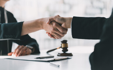 Close-up view of wooden hammer and lawyer with client shaking hands behind