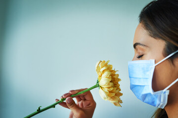 Poster - I cant seem to smell anything. Shot of a young woman smelling a flower while wearing a surgical mask.