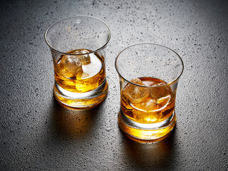 Wall Mural - Two glasses of elegant whiskey with ice on black textured background.