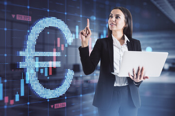 Wall Mural - Attractive happy european businesswoman holding laptop with abstract glowing growing forex chart and euro currency sign on blurry office interior background. Trade, finance and economy concept. 