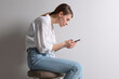 © New Africa - Woman with bad posture using smartphone while sitting on stool against light grey background
