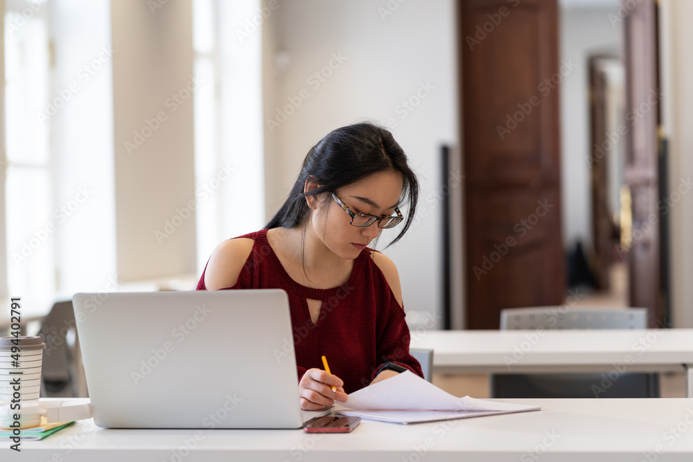 Girl Writing Assignment Young student girl making homework in library. Asian female writing ...