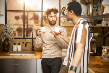 Two guys of different ethnicity having warm conversation while drinking coffee on kitchen at home. Concept of close male friendship or relationship as gay couple. Caucasian and hispanic man together