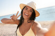 © Syda Productions - people, summer and swimwear concept - happy smiling young woman in bikini swimsuit and straw hat taking selfie on beach and showing peace gesture