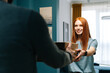 © dikushin - Pretty redhead young woman receiving paper boxes with hot pizza from unrecognizable courier male on doorway at home. Rear view of delivery man delivering boxes with food to female client at apartment.