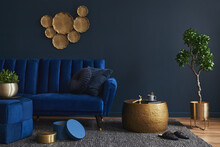 Elegant Modern Living Room Interior Design With Glamour Blue Velvet Sofa, Pouf, Golden Metal Side Table, Plants And Modern Home Accessories. Dark Blue Wall. Template. Copy Space..