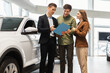 © Prostock-studio - Confident car salesman showing purchase details to young Caucasian couple at dealership center
