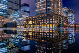 Fototapeta Miasto - CHIYODA, TOKYO, JAPAN - MARCH 22, 2022 : Night city view of business buildings around the Marunouchi side of Tokyo Station after rain. Reflection photo with beautiful specular reflection.
